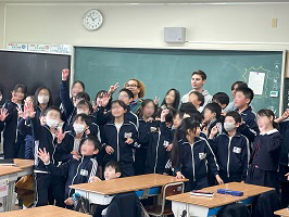 黒板前で集合写真を撮る留学生と児童たち